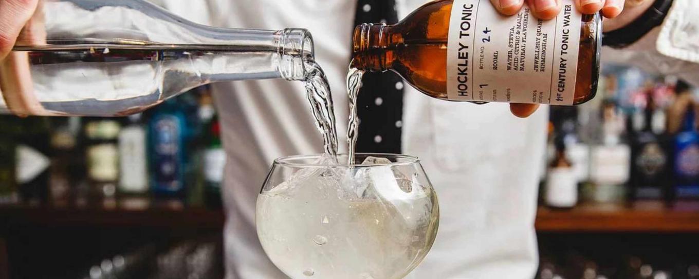 A barman pouring a gin and tonic into a glass