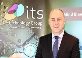 A man in a suit smiling in front of a ITS Technology Group branded wall