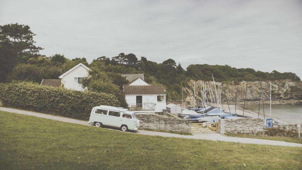 A camper van on a quiet street with boats and hills in the background