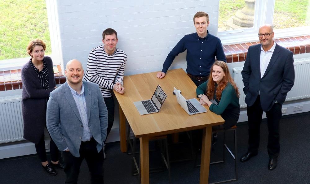 Employees from Collabor8 gathered around a table smiling with 2 laptops in front of them