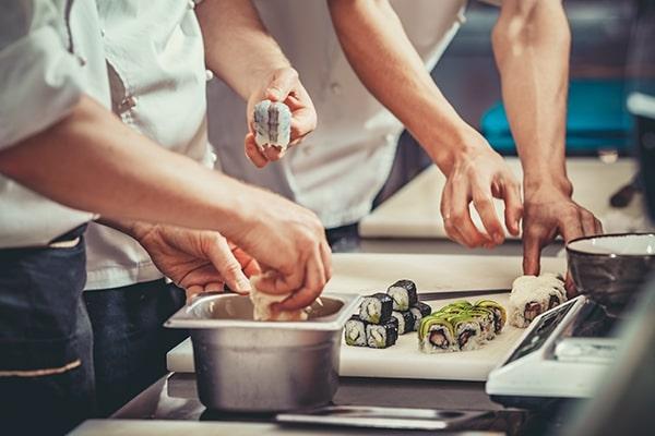 The hands of three cooks preparing sushi rolls