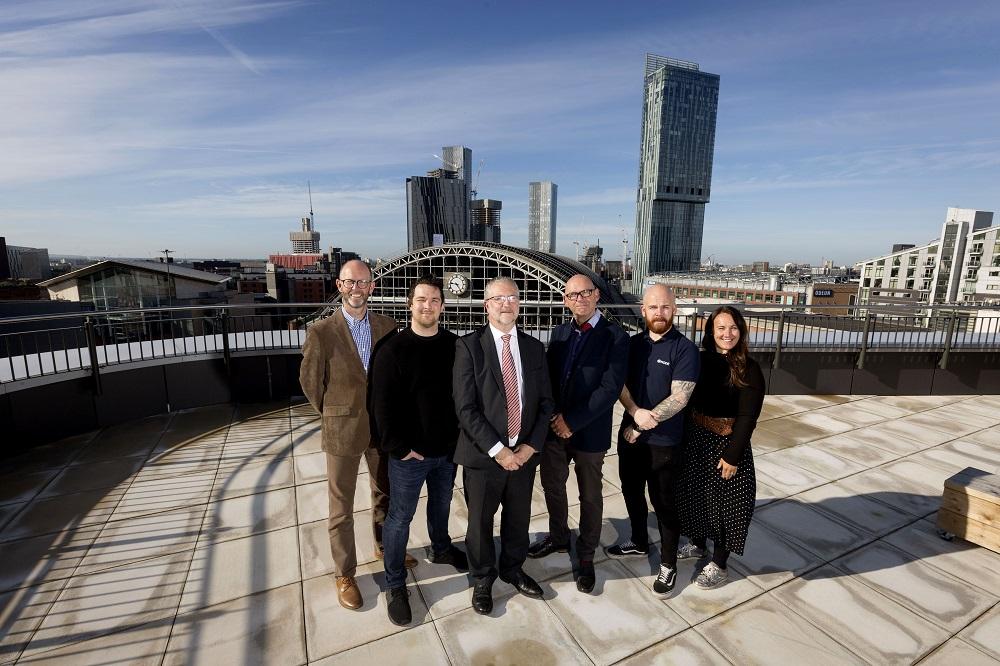 A group of employees from Node Technologies stood outdoors with the city of Manchester in the background