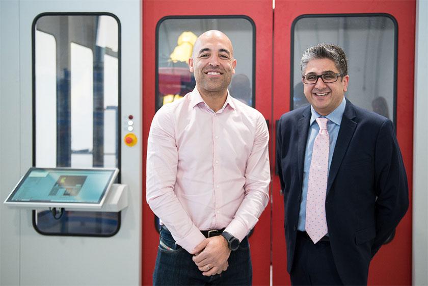 Two men stood in front of red doors with a control panel next to the doors