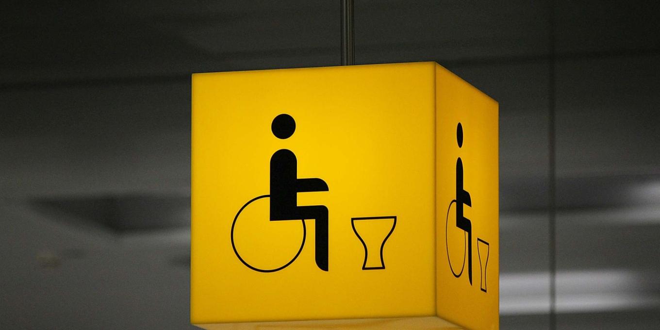 A yellow cube sign, lit up with an icon of a person in a wheel chair and a toilet silhouette
