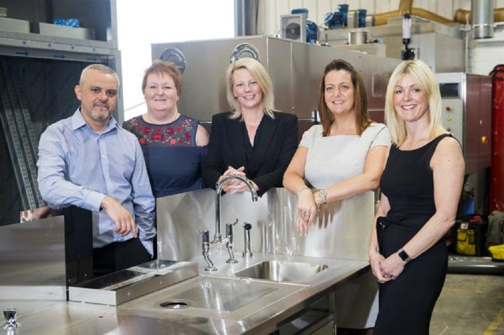 A man and four women in a warehouse environment stood around a sink area