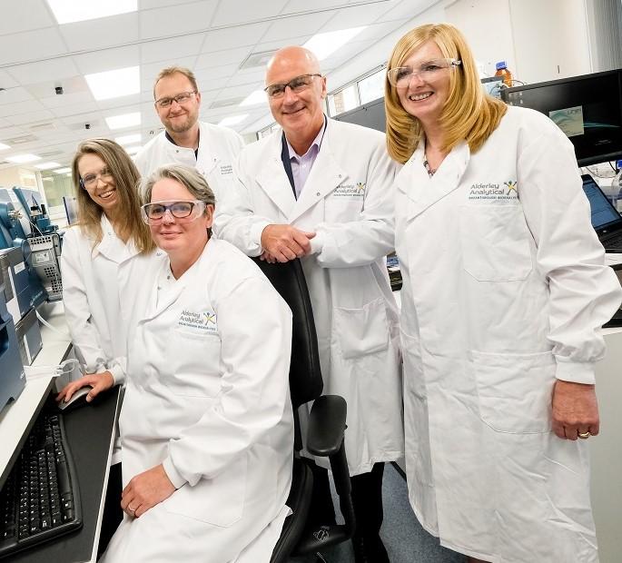 Three women and two men wearing white lab coats in a laboratory