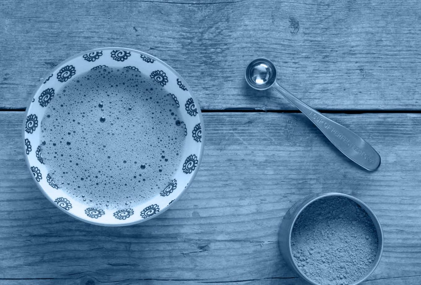 A cup of tea on a wooden table with a metal spoon next to it