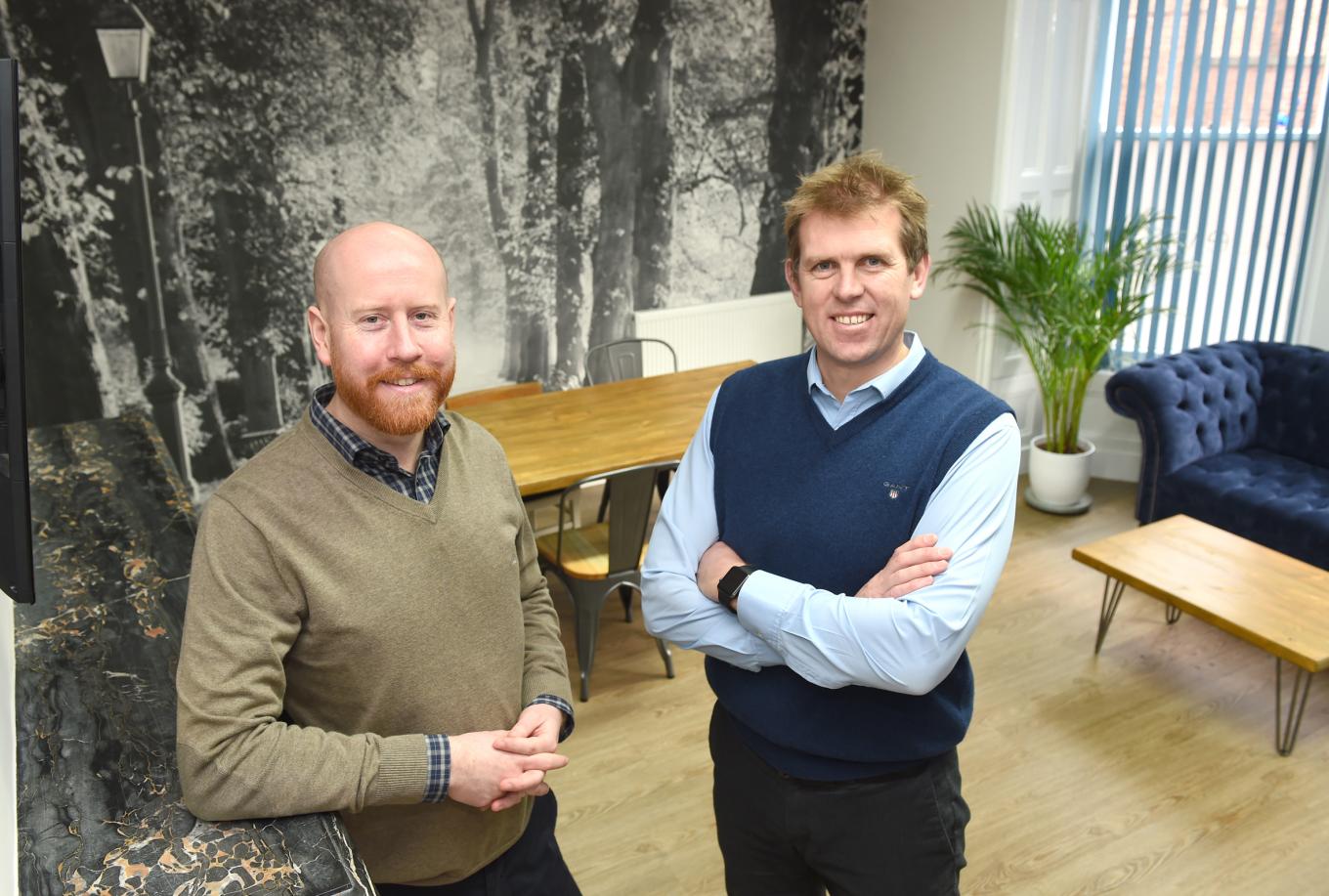 2 men from Blue Wren stood in an office with tables, chairs and a sofa in the background