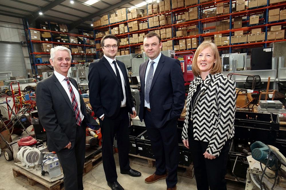 3 men and a woman smiling and stood in a warehouse