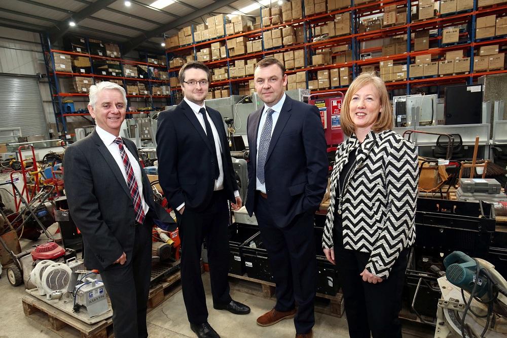 3 men and a woman smiling and stood in a warehouse