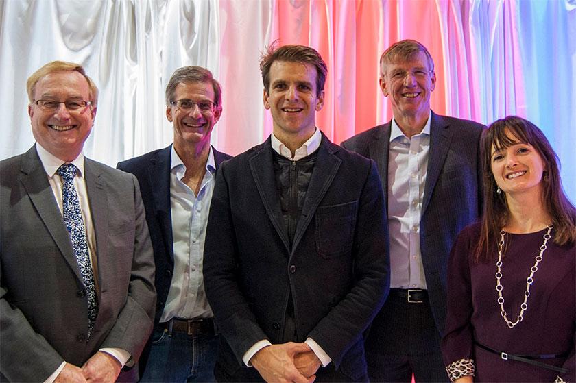 4 men and a woman stood smiling in front of a multi coloured background