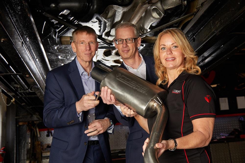 2 men and a woman from Cobra Sports stood under a car holding an exhaust