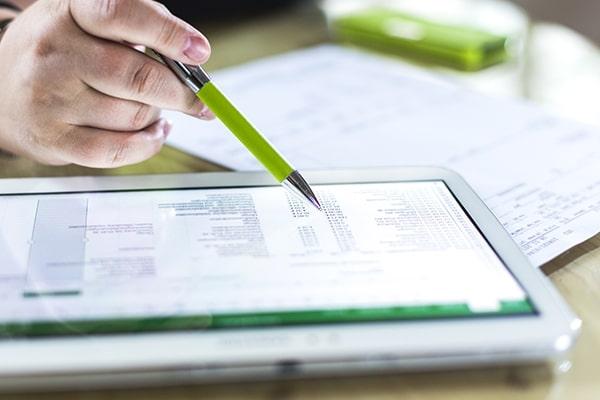 Close-up of a tablet with software on screen, above which is a person's hand holding a green pen