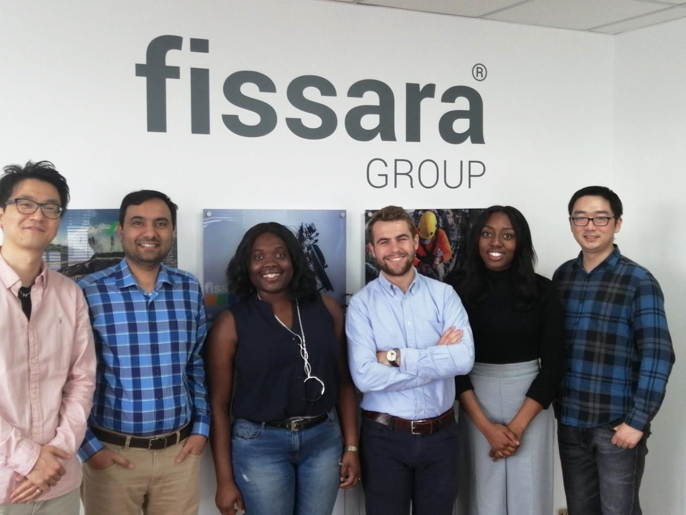 A group of employees smiling and stood in front of a Fissara Group branded wall