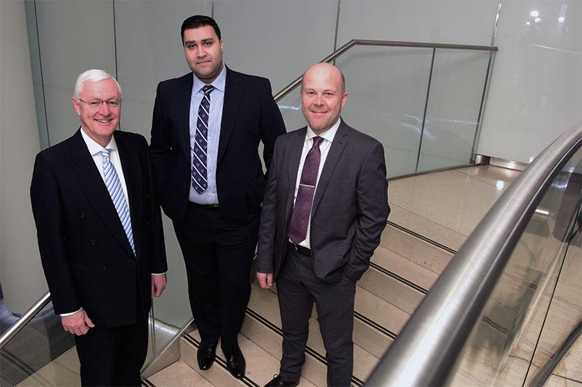 3 men in suits smiling and stood on some stairs in an office building