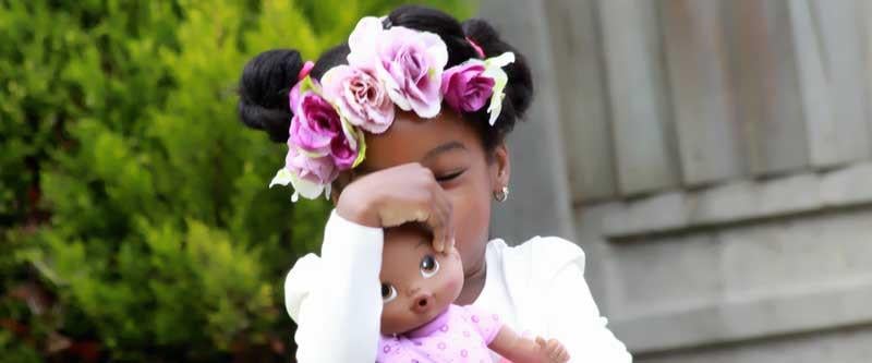 A young girl with flowers in her hair holding a doll