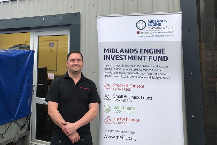 A man from GHO Pressings stood outside of an office building with a Midlands Engine Investment fund pop up banner next to him