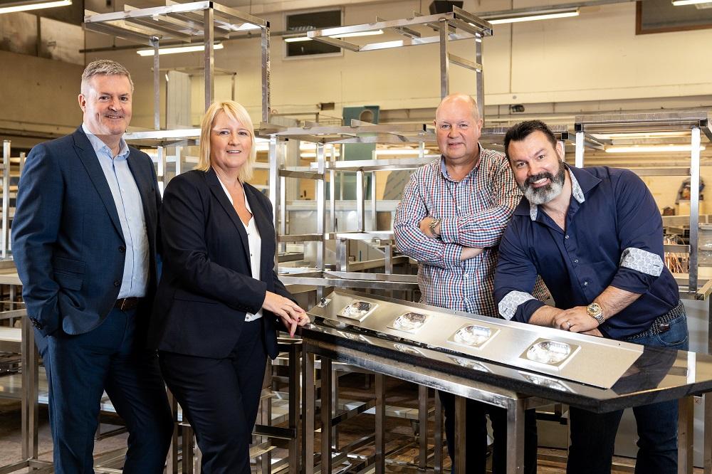 3 men and a women stood in a kitchen surrounded by metal catering equipment