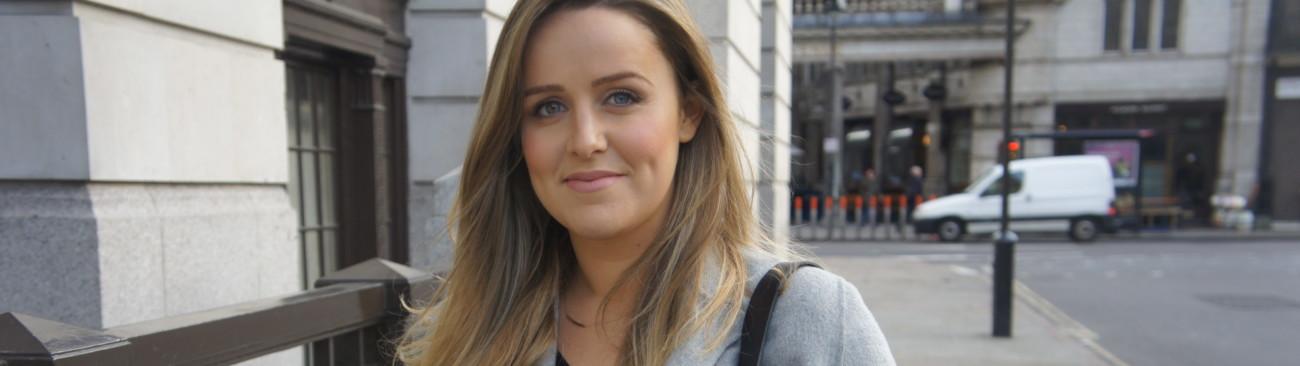 A close up of a women smiling outside with the street in the background