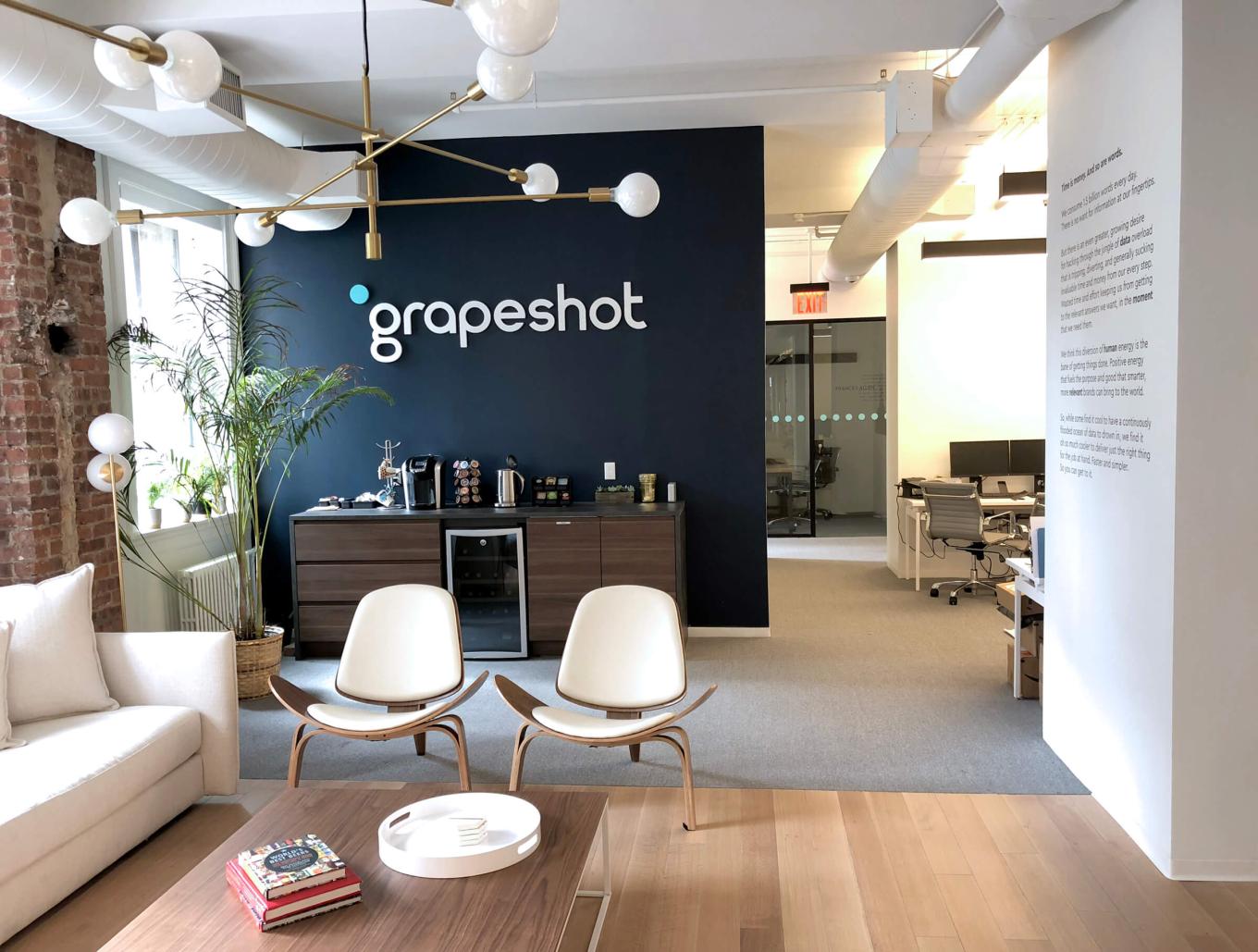 An office seating area with the Grapeshot logo on the wall and tea and coffee making facilities in the back