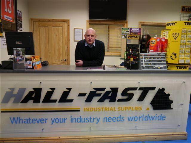 Malcolm Hall MBE, managing director of Hall-Fast Industrial Supplies, standing behind the counter at his company's store