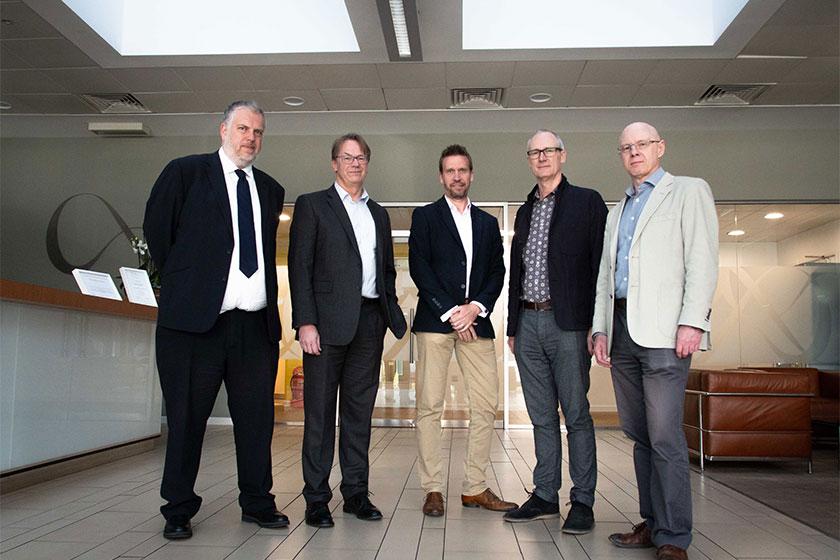 5 men in suits smiling and stood in the reception area of an office