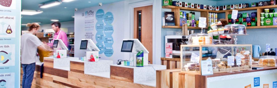 Tills and a cake counter in an independent supermarket with one customer paying