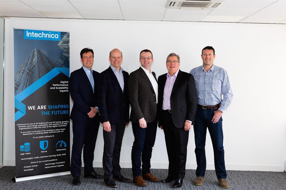 5 men in suits smiling and stood in an empty meeting room with a Intechnica pop up banner next to them