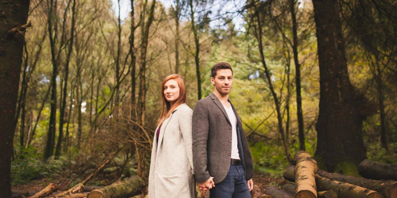 A man and a woman holding hands and posing in a forest