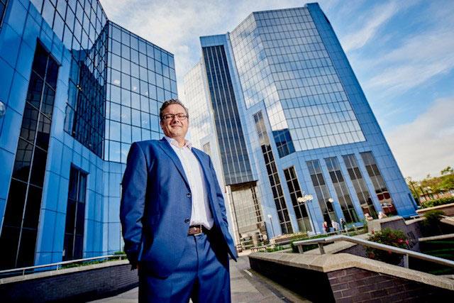 A man in a suit with his hands in his pockets stood in front of tall glass buildings