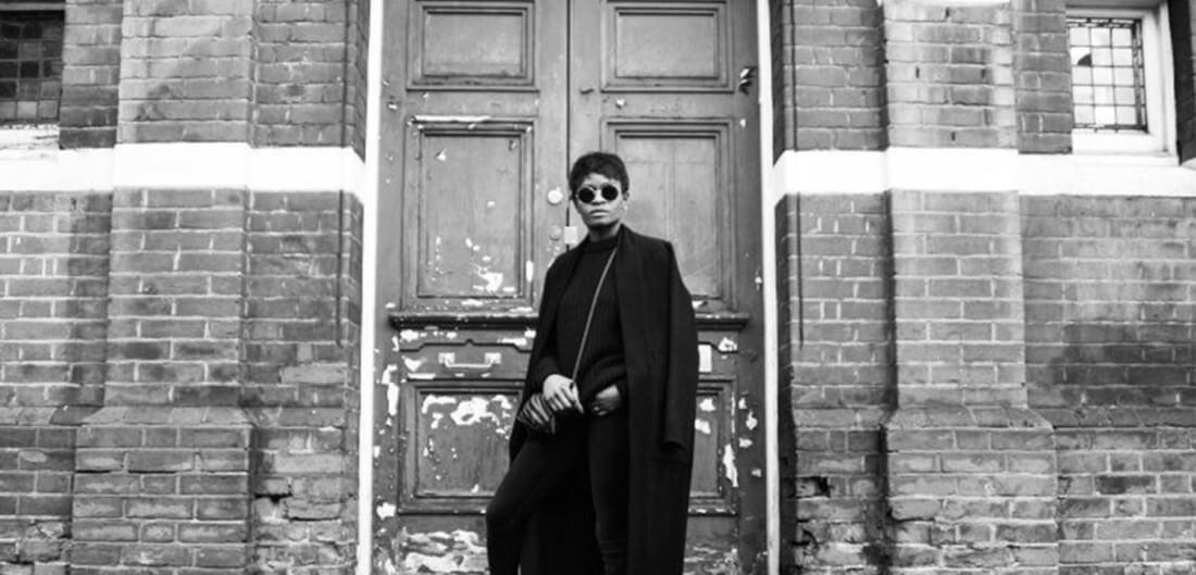 A man dressed in black with sunglasses posing outside of an old building