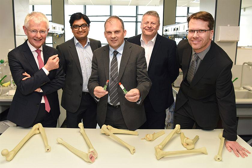 5 men in suits stood around a table of plastic bones