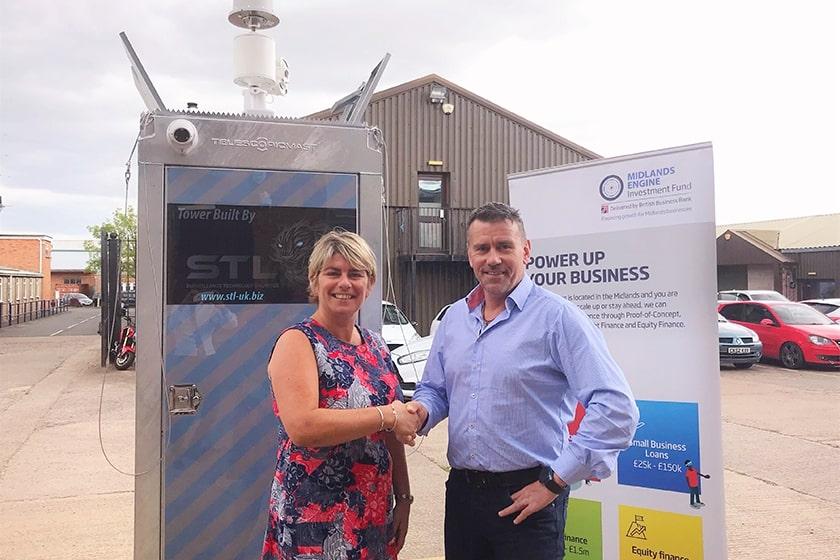 A man and a women shaking hands in a car park with surveillance equipment and a MEIF pop up banner behind them