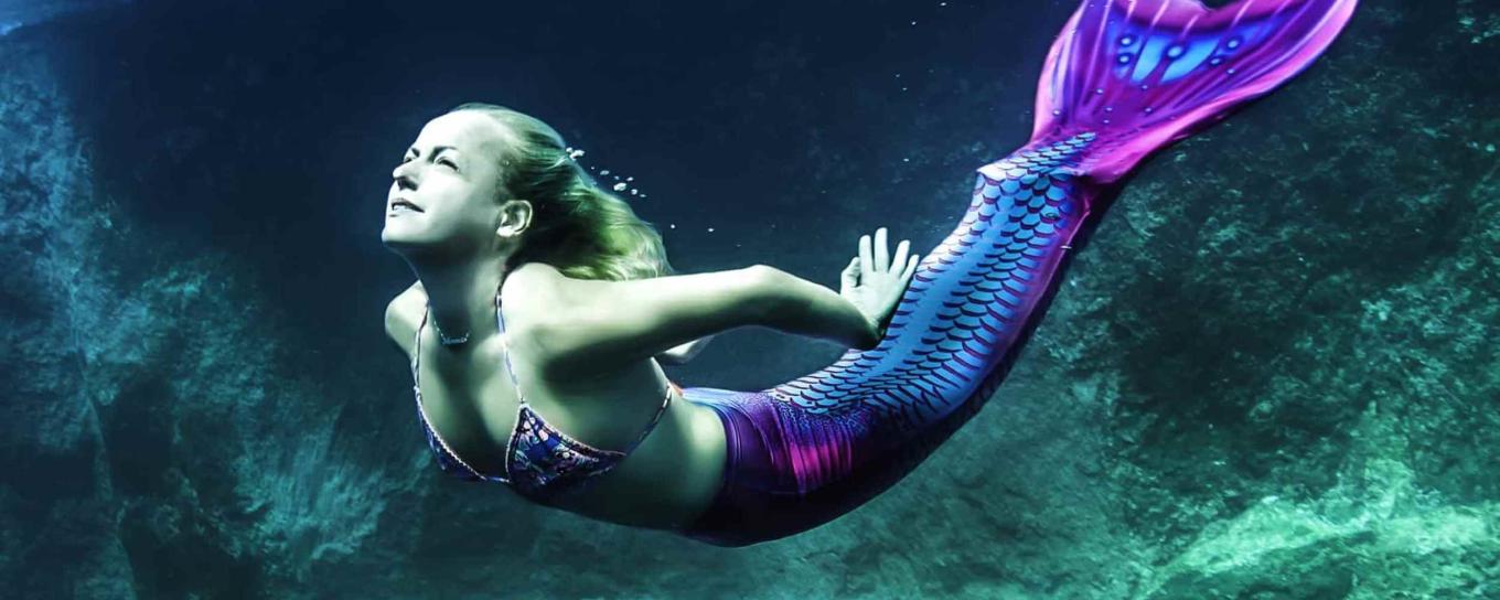 A woman dressed as a mermaid in the water with rocks in the background