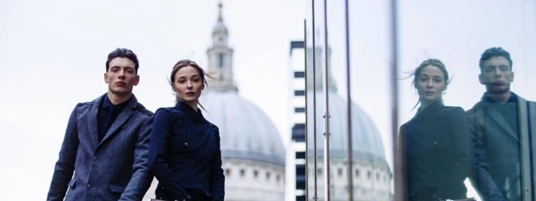 A man and a women dressed in black posing next to a glass building with St Pauls Cathedral in the background