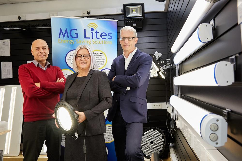 2 men and a woman stood around energy saving equipment with an MG Lites Energy Saving Solution pop up banner in the background