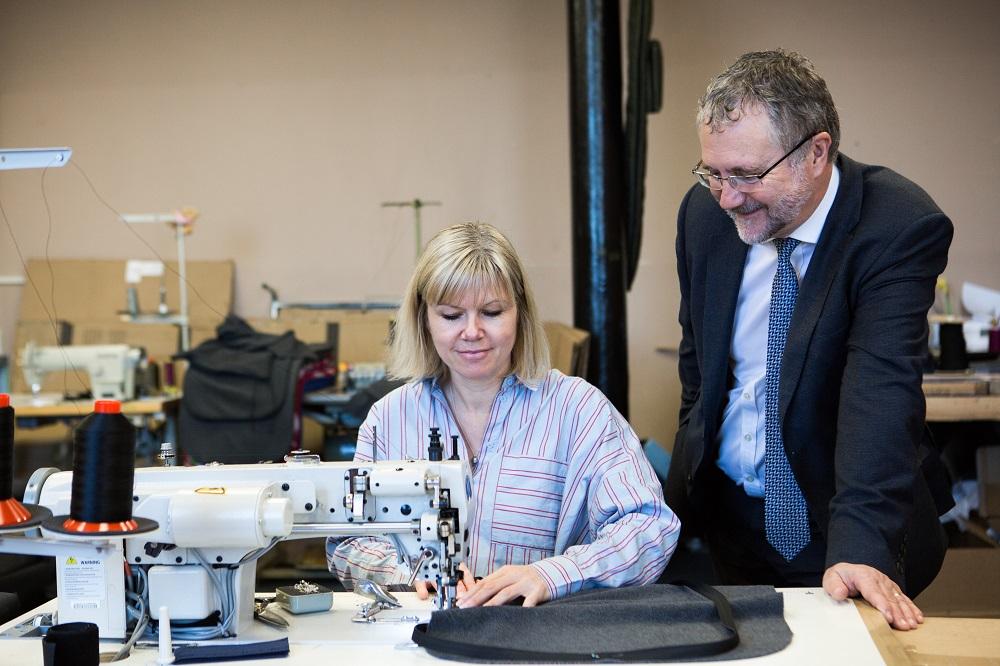 A man stands next to a woman as she is sewing some fabric on a sewing machine