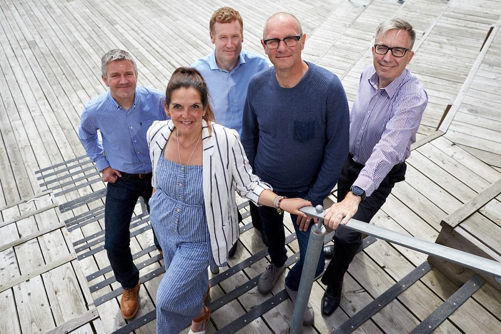 4 men and a woman smiling and stood on some wooden stairs