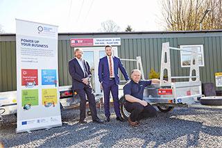 3 men stood outdoors near some trailer equipment with a Midlands Engine Investment Fund pop-up banner next to them