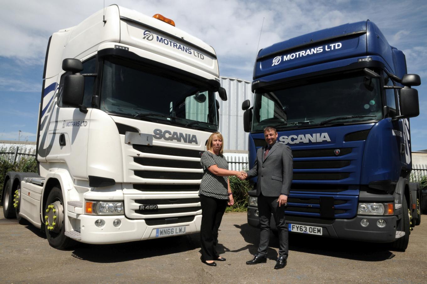 A man and a women shaking hands in front of 2 Motrans lorries