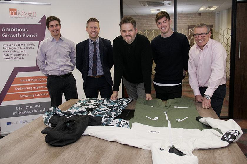 5 men from Oneskee stood in a meeting room with snow sports apparel on the table in front of them