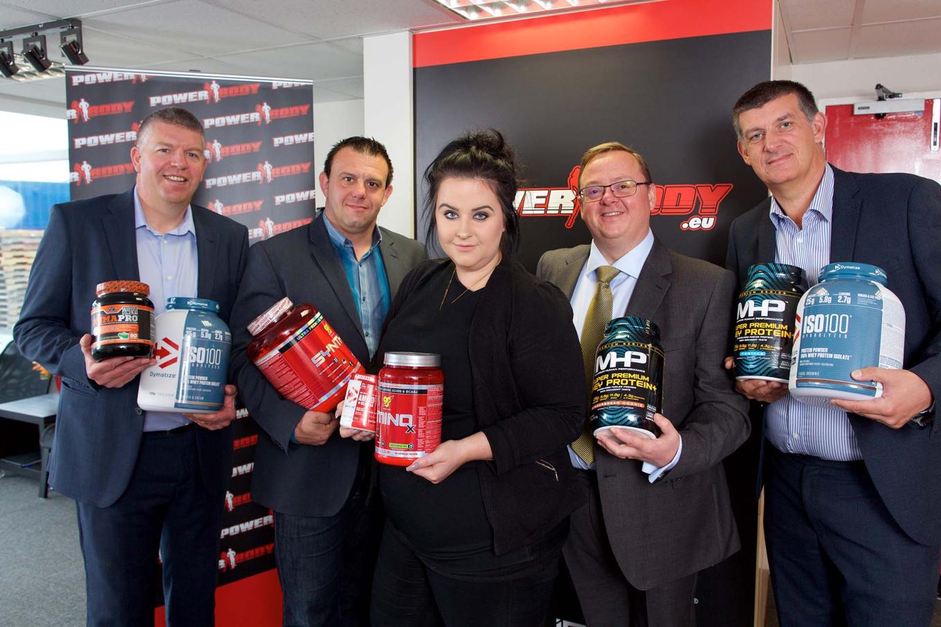 Employees from Power Body Nutrition stood in front of a branded pop up screen holding protein powder tubs