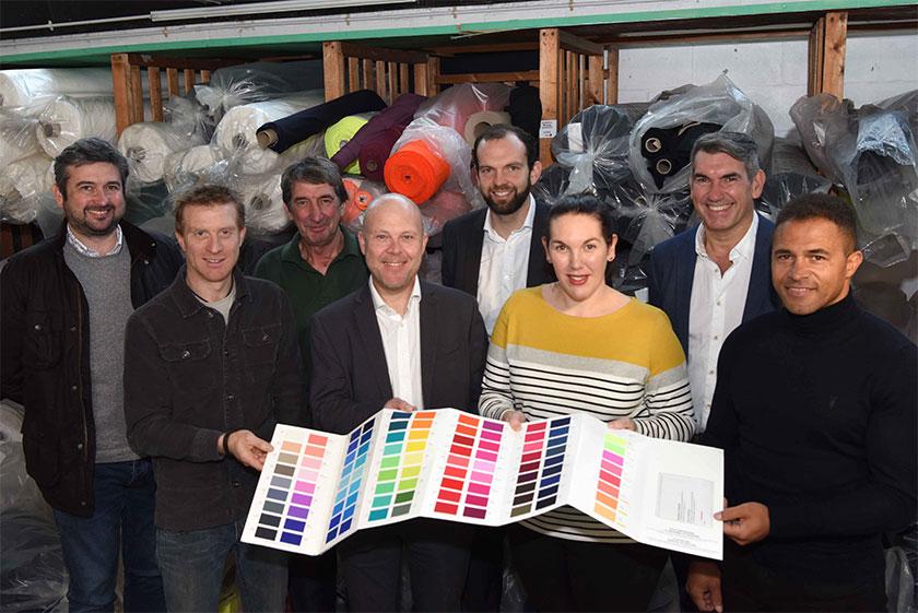 Employees from Proskins holding a colour swatch book with rolls of fabric in the background