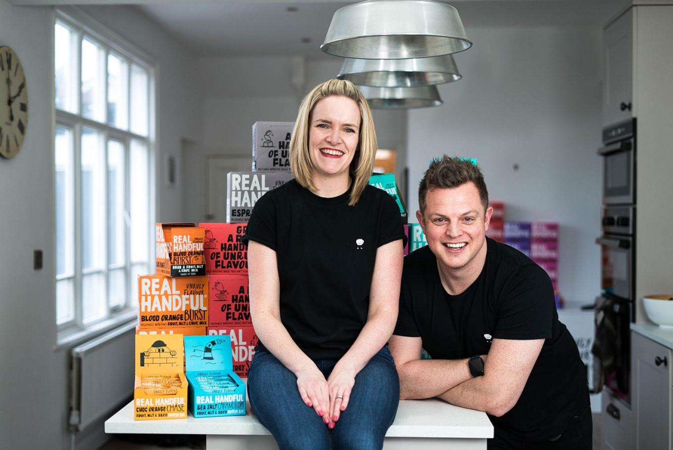 A man and woman from Real Handful with a table full of their healthy snacking products