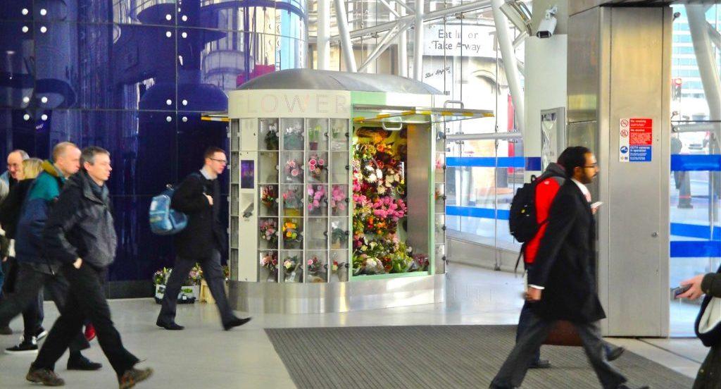 Commuters walking past a Rockflower kiosk at the exit of a London Underground station