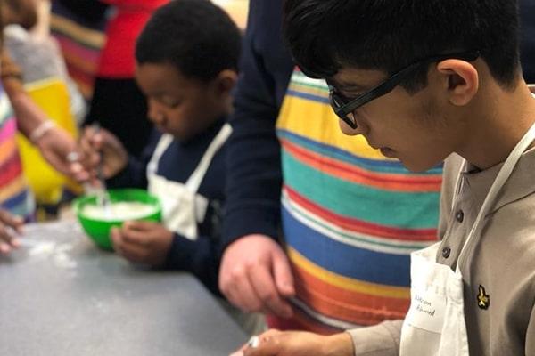 A young blind boy with glasses taking part in a cookery activity alongside an adult teacher
