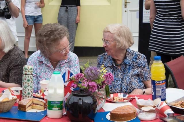 2 women sat at a union jack themed table having tea and cake whilst chatting