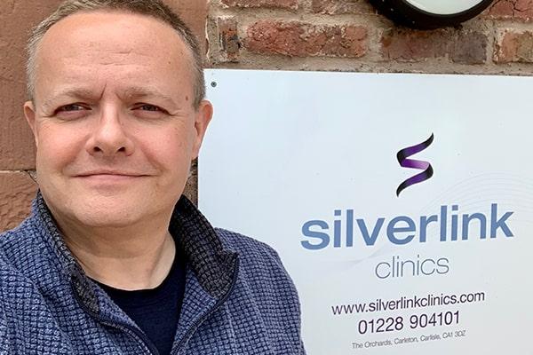 CEO of Silverlink Clinics standing beside his company's nameplate fixed to the exterior of the clinic