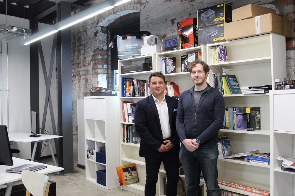 2 men from Simul Software stood in an office with a shelves of books and boxes in the background