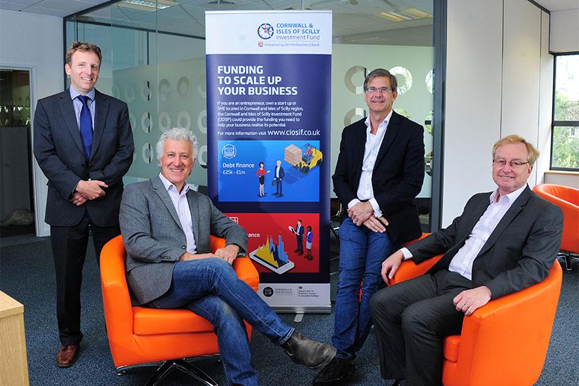 Four men in suits in a Swoop Applications office with a Cornwall and Isles of Scilly Investment Fund banner